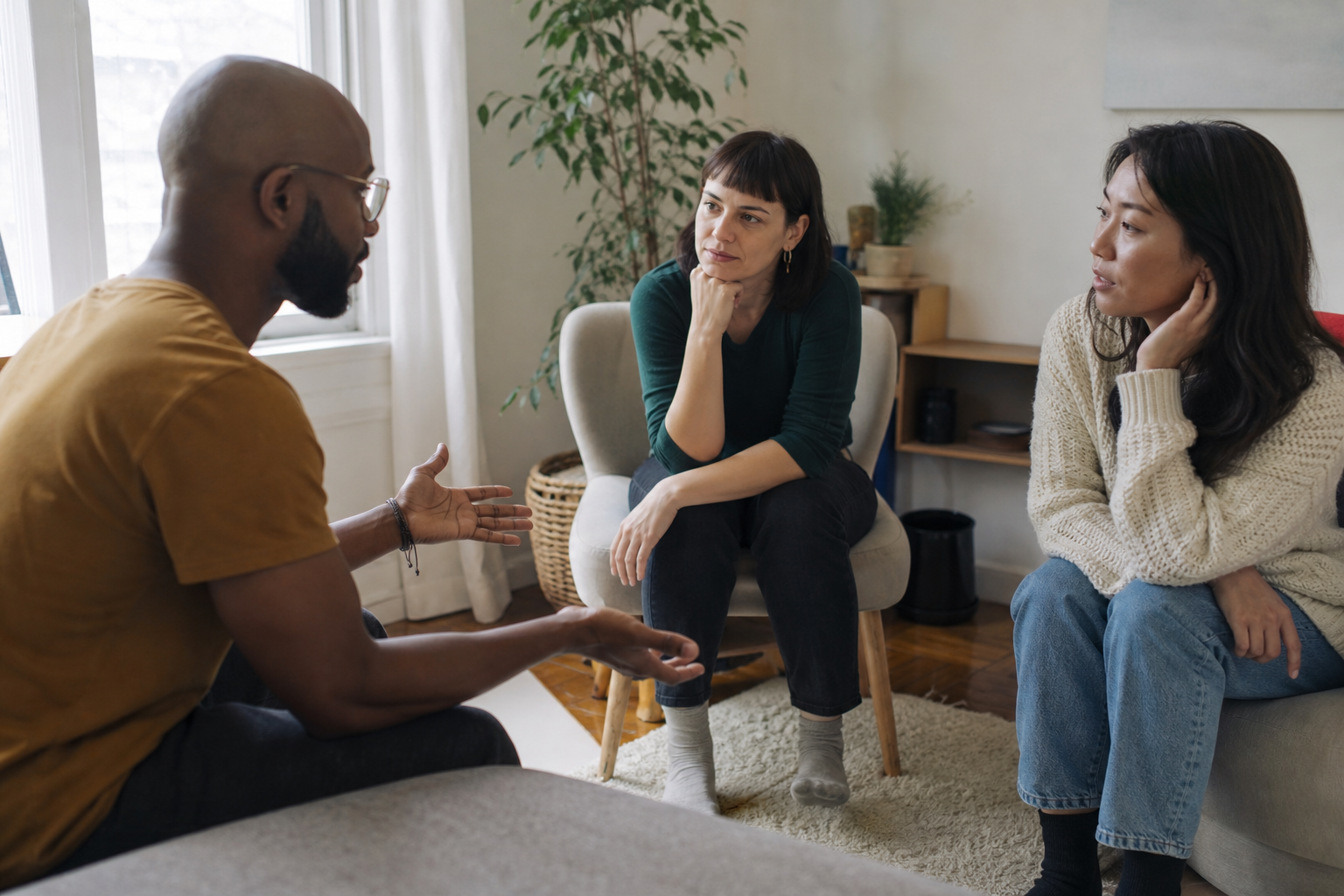 Três adultos conversam com seriedade em uma sala, ouvindo uns aos outros.