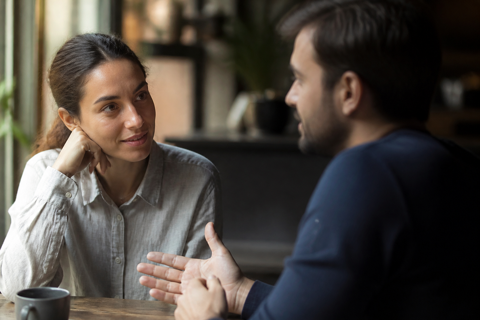 Uma pessoa observa atentamente as expressões e os gestos de alguém durante uma conversa em um café.